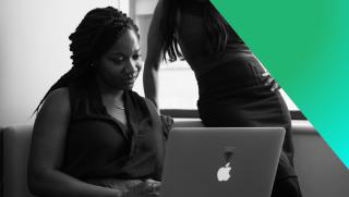 Black and white photography of two female IT professionals looking at a laptop.